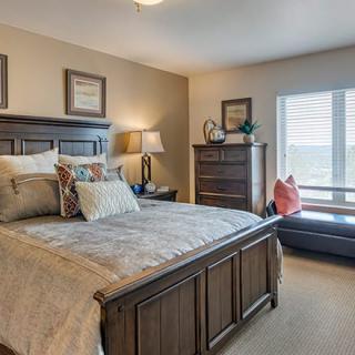 A cozy and well-decorated bedroom with a large wooden bed, stylish pillows, and a dresser near the window.