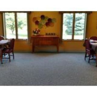 A cozy dining room with tables and chairs, decorated with wall art and a side table near the windows.