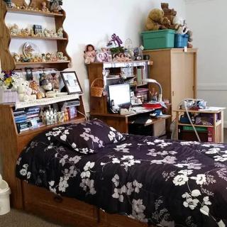 A cozy bedroom featuring a single bed with a floral bedspread, surrounded by shelves filled with decorations and stuffed animals.