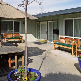 A cozy outdoor patio area with wooden benches, an umbrella, and potted plants.