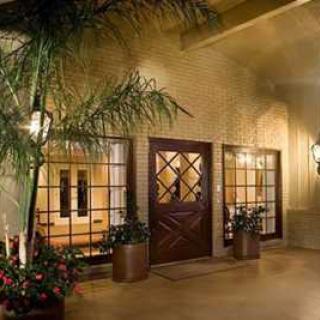A warmly lit building entrance with glass doors and windows, adorned by potted plants.