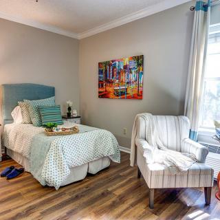 A cozy bedroom with a single bed, armchair, and colorful wall art.
