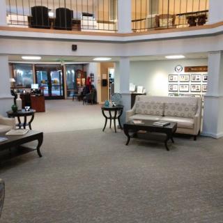 A spacious lobby area with sofas and tables, featuring a carpeted floor and visible reception desk.