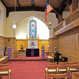 Interior view of a church with an altar, stained glass window, and seating.