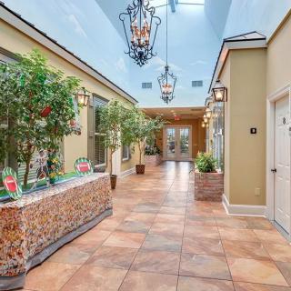 A bright hallway featuring decorative plants, chandeliers, and tiled flooring.