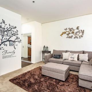 A cozy living room with a gray sofa, wall art featuring a family tree decal, and decorative cushions on a plush rug.