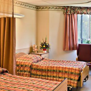 A shared hospital room with two beds, a privacy curtain, and a window with curtains.