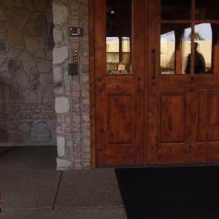 A stone-walled building entrance featuring wooden doors with glass panels reflecting the surroundings.