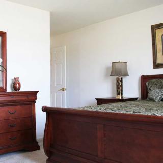A neatly arranged bedroom with a wooden bed frame and dresser, featuring elegant decor.
