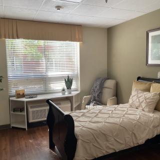 A cozy and neatly arranged bedroom with a single bed, armchair, and window with blinds.
