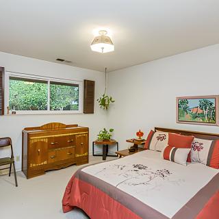 A cozy bedroom with a neatly made bed and a wooden dresser beside a window.
