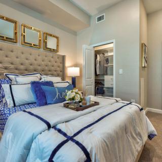 A modern bedroom with cozy decor, featuring a plush bed adorned with blue accents and a view into a walk-in closet.