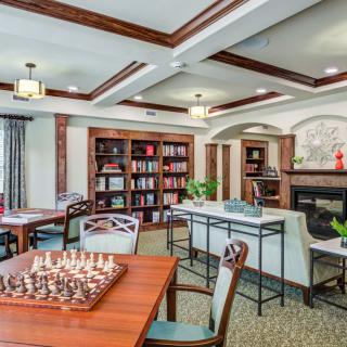 A cozy library room with bookshelves, a chessboard on a table, and comfortable seating.