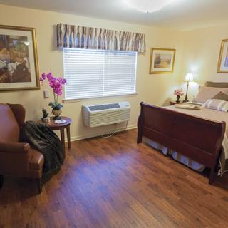 A cozy bedroom with wooden flooring, featuring a bed, chair, and decorative elements.