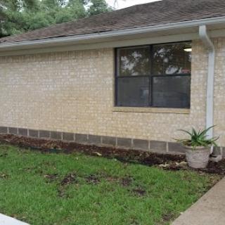 A side view of a house featuring a window, brick foundation, and newly landscaped area with grass and plants.