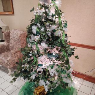 A beautifully decorated Christmas tree featuring white and green accents, surrounded by a cozy indoor setting.