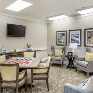 A cozy living room area with seating and a table for games, featuring wall-mounted artwork and a television.