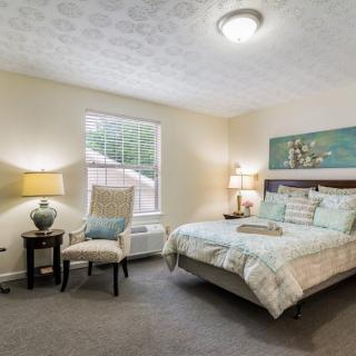 A cozy bedroom with a bed, two lamps, a chair, and a window.