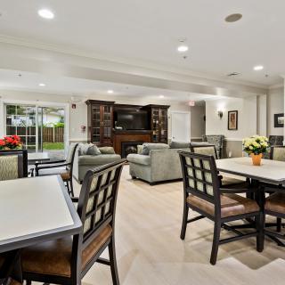 A spacious and well-lit living area featuring comfortable seating, a television, bookshelves, and dining tables.