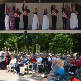 A patriotic performance takes place on stage as an audience, including veterans, watches attentively outdoors.