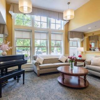 A cozy living room with modern decor, featuring a grand piano, comfortable couches, and large windows bringing in natural light.
