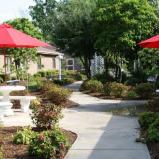 A scenic garden with a winding pathway and outdoor seating under red umbrellas.
