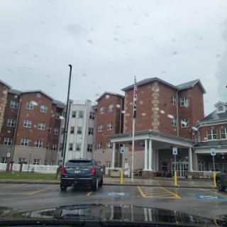 A view of a hospital building on a cloudy day, with a vehicle parked in front.