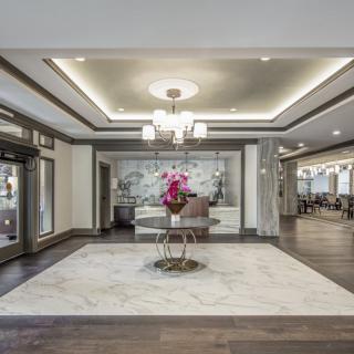 A modern lobby with elegant interior design, featuring a chandelier and a table with flowers on marble flooring.