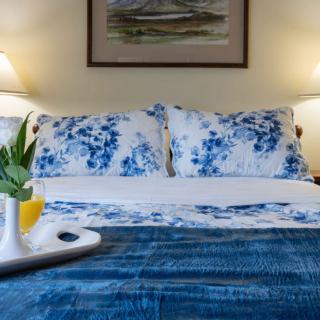 A cozy bedroom setup featuring a bed with blue and white floral pillows, a matching comforter, and a tray with a drink and plant on top. The space is warmly lit by lamps on either side.
