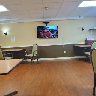 An empty dining area featuring tables and chairs, with a television mounted on the wall.