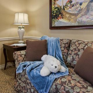 A cozy living room with a floral sofa, accented by a blue blanket and stuffed bear, set beside a lamp and painting.
