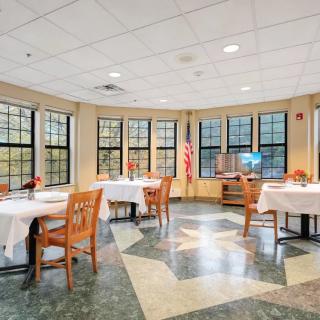 A well-lit dining area with neatly arranged tables and chairs, surrounded by large windows.