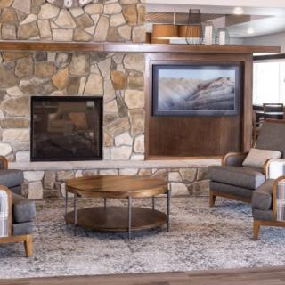 A cozy living room features a stone fireplace, modern armchairs, and a stylish coffee table on a patterned rug.