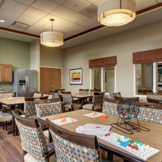 A modern dining room with neatly arranged tables and chairs, contemporary lighting fixtures, and an adjoining kitchen area.