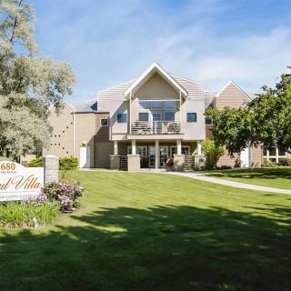 A modern house with a large lawn and surrounding trees under a clear blue sky.