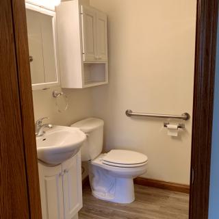 A small, accessible bathroom with a toilet, sink, and mirror cabinet.