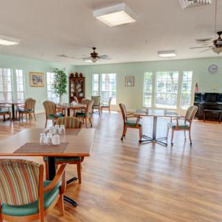 A spacious and bright dining area with multiple tables and chairs, featuring large windows and a wooden floor.