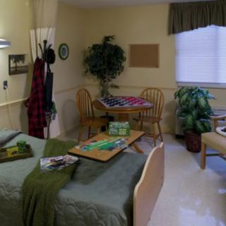 A cozy hospital room with a bed, table, chairs, and decorative plants.
