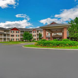 A large, multi-story residential building surrounded by greenery and a clear blue sky.