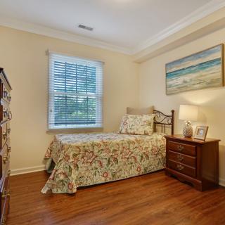 A cozy bedroom with a single bed, wooden dresser, and a beach-themed painting on the wall.