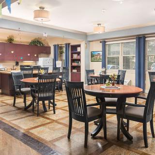 A spacious dining area with round tables and chairs, featuring a kitchen space in the background.