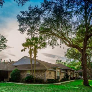 A suburban house surrounded by trees and a well-maintained lawn under a partly cloudy sky.