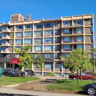 A modern residential building with multiple balconies and greenery in the foreground.