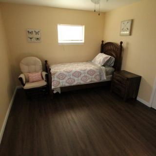A minimalist bedroom featuring a single bed, a chair, and a nightstand on a dark hardwood floor.