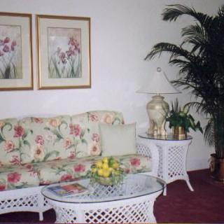 A cozy living room featuring a floral-patterned couch, glass-top coffee table with a bowl of lemons, and decorative framed artwork on the wall.