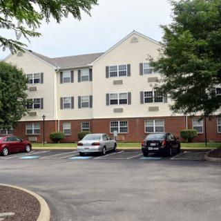 A view of a three-story apartment complex with parked cars and surrounding greenery.