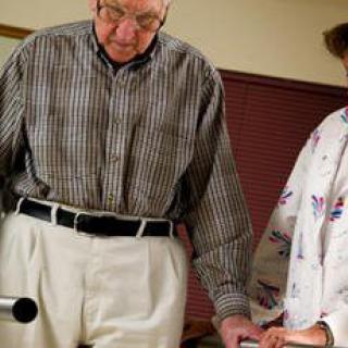 An elderly person receiving support with a walking aid.