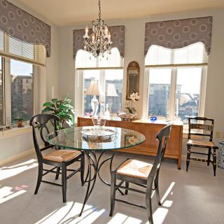A bright dining area with a glass table, black chairs, and large windows letting in natural light.