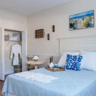 A cozy and well-decorated bedroom with a neatly made bed, wall art, and a robe hanging in an open closet.