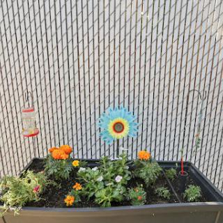 A vibrant raised garden bed filled with colorful flowers and a decorative flower stake against a textured wall.